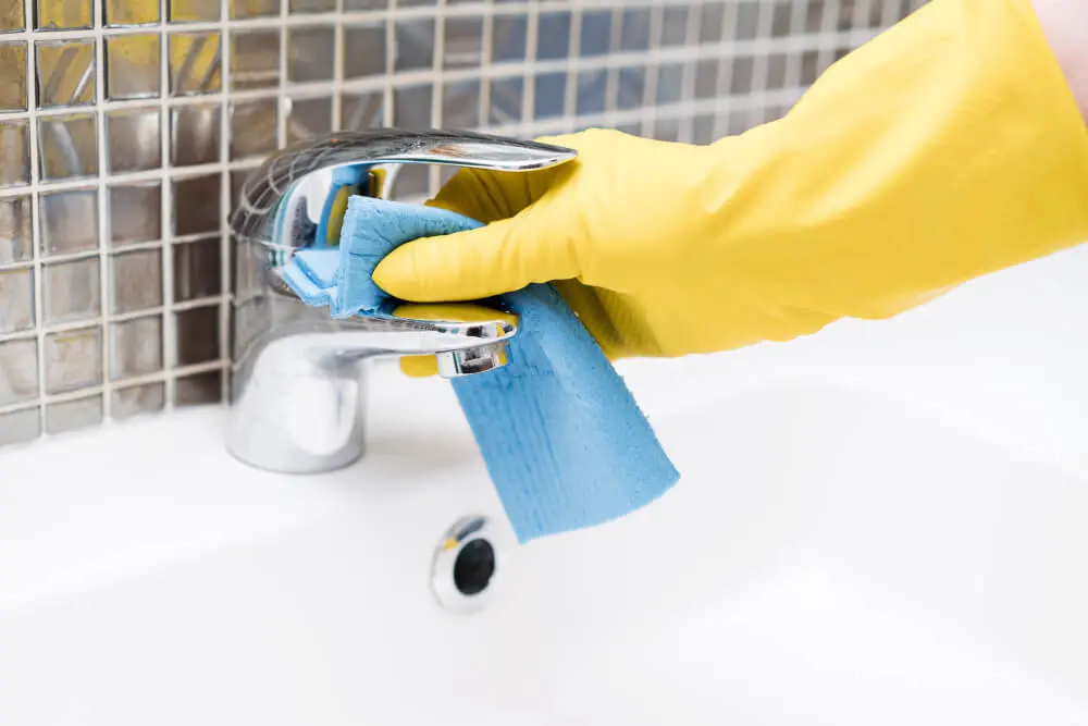 person wiping down stainless steel faucet