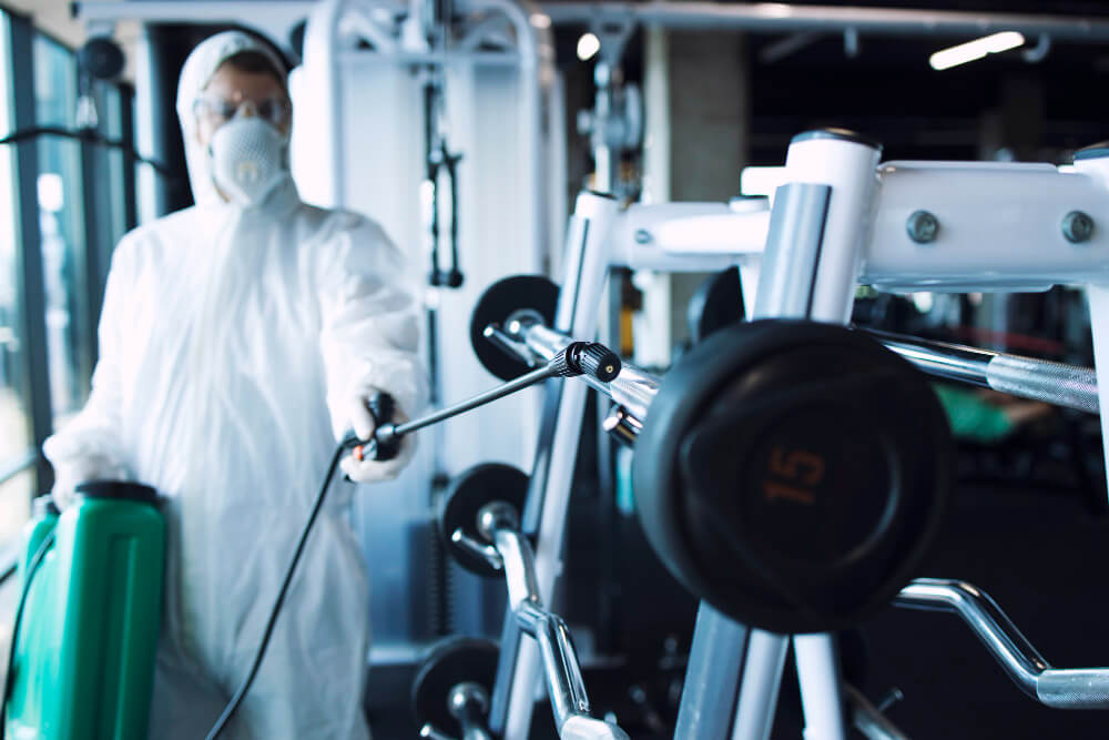 man wearing a white hazmat suit using a fogging equipment to clean a barbell