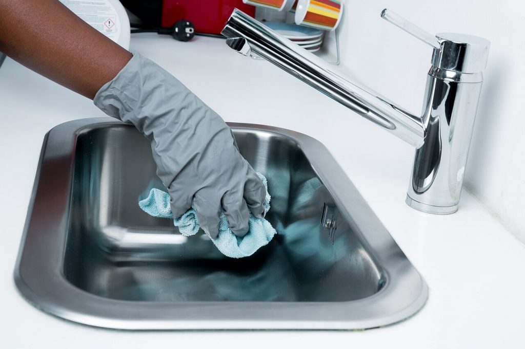 hand wearing gloves cleaning a stainless steel sink with a blue cloth