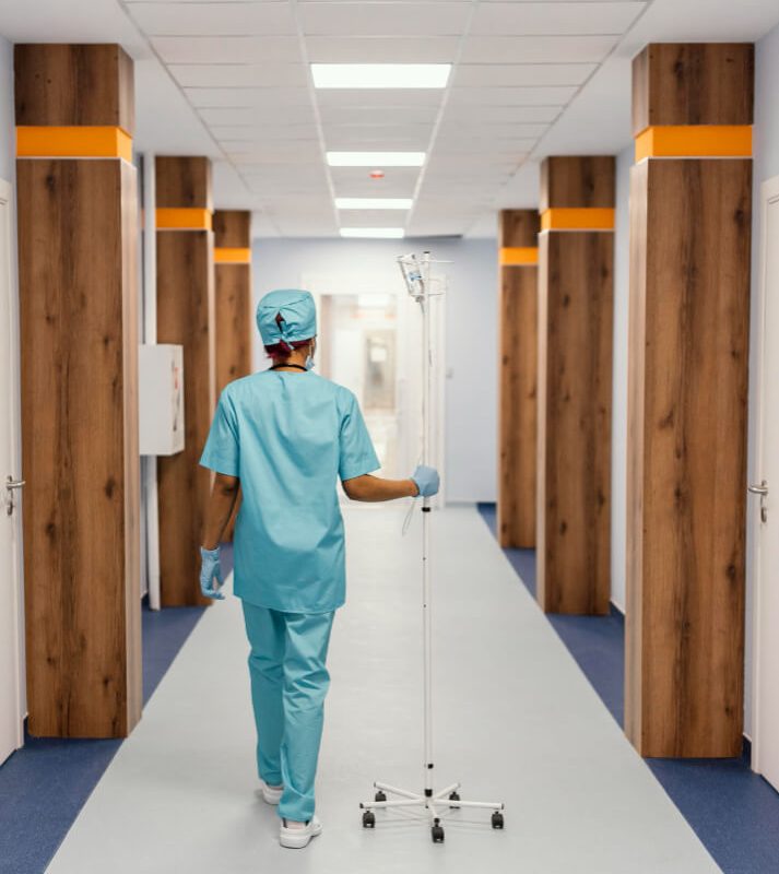 nurse with an iv pole walking in a hospital hallway