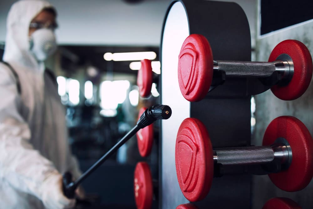 man disinfecting dumbbell racks in fitness center