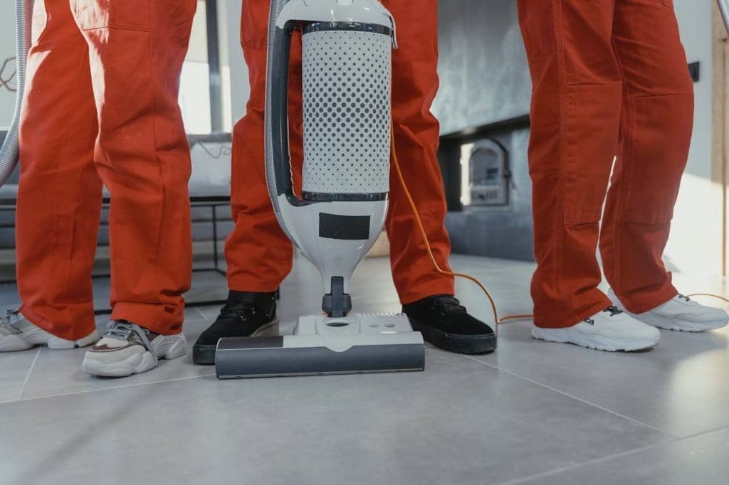 below the waist images of 3 people wearing red jumpsuits and standing behind cleaning equipment