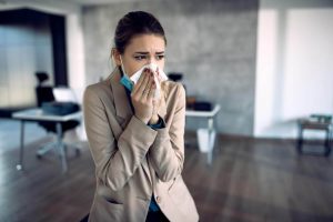 Sick businesswoman blowing nose while working in the office