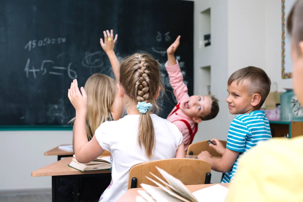students raising hands for recitation in classroom