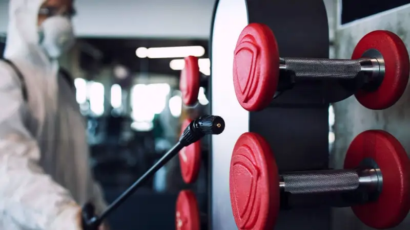 Cleaning technician disinfecting dumbbell racks in fitness center in Fort Worth TX