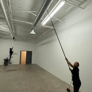 Crew high dusting light fixtures and ventilation ducts in warehouse